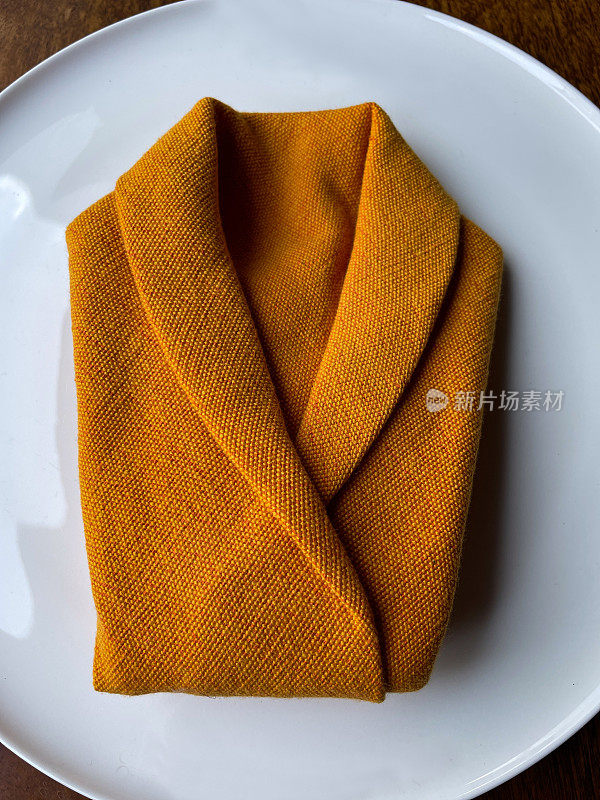 橙色布餐巾在白色瓷盘上的股票图像，西装外套折叠织物servviette，布在桌子上的升高的观点