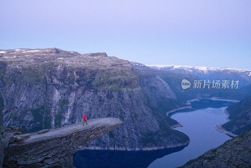 男性徒步旅行者站在巨魔之舌(trollltunga)著名的岩石上，俯瞰湖面上的山谷全景，是挪威著名的探险之旅