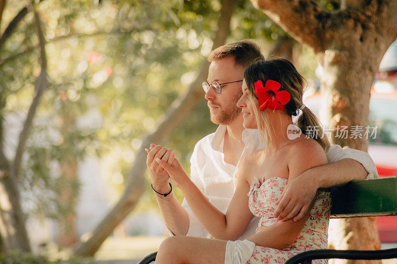 年轻的男人看着他美丽的女朋友的手，而他们正坐在公园的长椅上