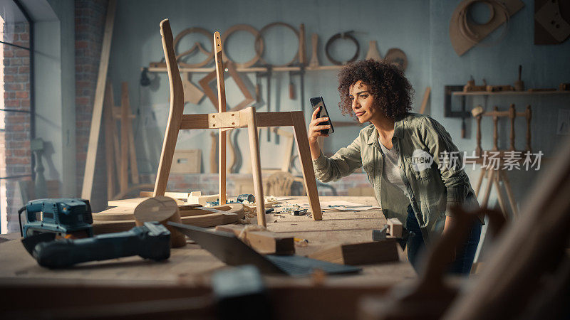 工匠产品设计师正在用智能手机拍摄木椅项目的照片。多民族创意女性上传照片到她的社交媒体档案，从粉丝和朋友的反馈。