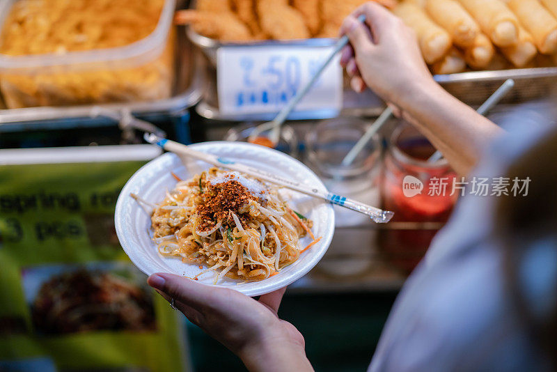 年轻的亚洲妇女在摊前给食物调味。