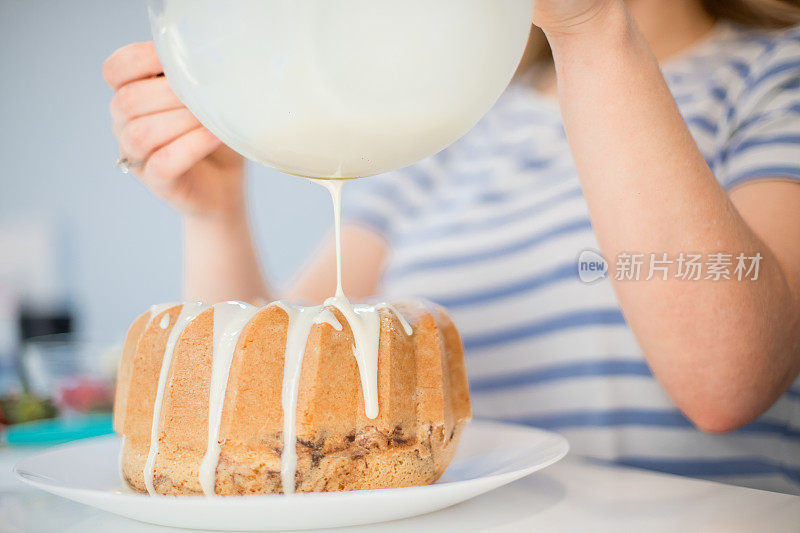 年轻女子正在装饰库格霍夫蛋糕，并把融化的白巧克力倒在上面