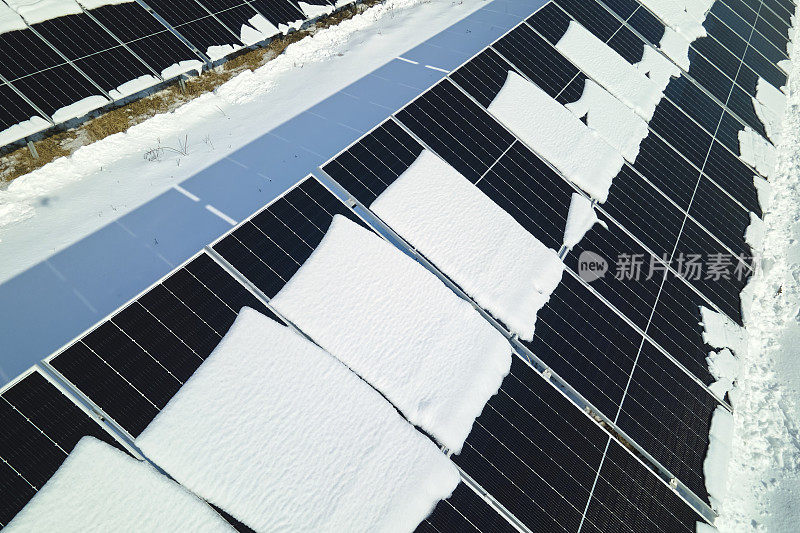 航拍的积雪融化覆盖太阳能光伏板在可持续发电厂生产清洁电力。冬季可再生能源发电效率低