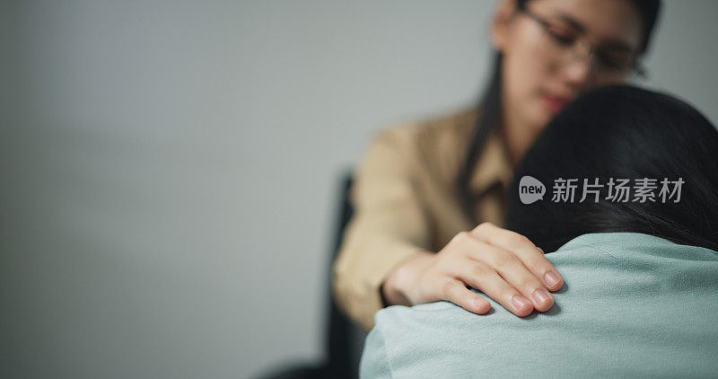 年轻的专业治疗师一边哭泣一边抚摸女病人的肩膀