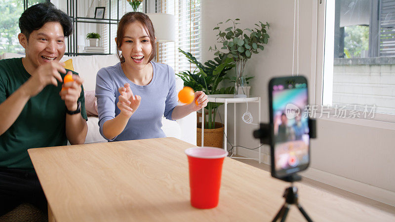 成人影响者youtuber亚洲人视频博主记录病毒视频视频博主页面直播有趣的游戏啤酒乒乓球扔杯子IG卷轴instagram抖音社交媒体时髦的快乐为年轻夫妇的副业。