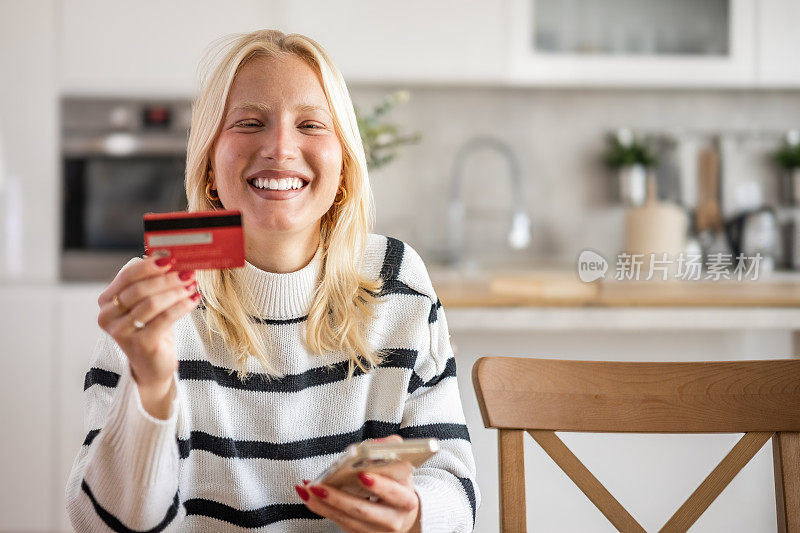 一位金发的年轻女子正在家里用手机和网上支付卡网购