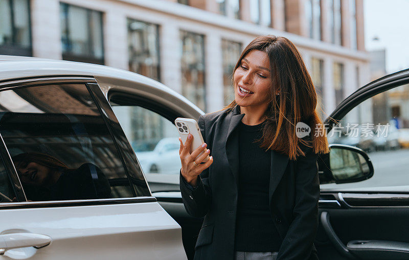 乐观的都市职业女性在城市的动态背景和她时髦的汽车衬托下，享受着轻松愉快的电话交谈