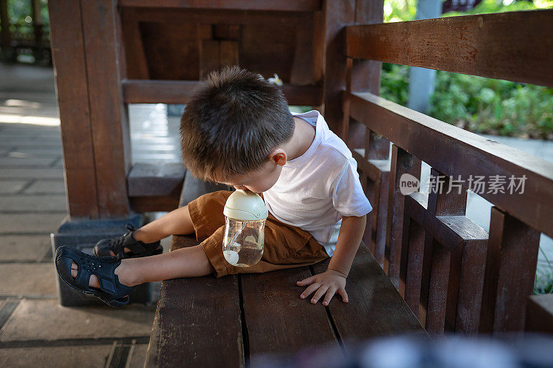 一个小孩在公园里从瓶子里喝果汁