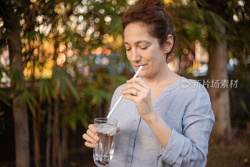 一名白人妇女用吸管啜饮冰水，这是敏感牙齿治疗系列的一部分