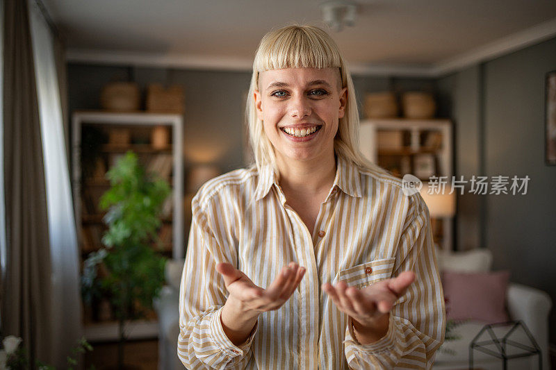 一名年轻女子站在客厅里为她的视频博客拍摄视频，看着镜头，在社交媒体上与她的粉丝交谈