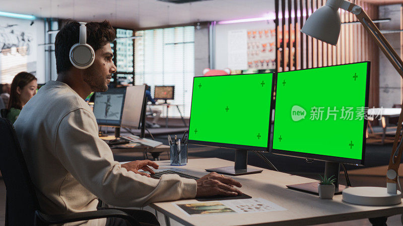 印度男性游戏设计师使用带有绿屏Chromakey的桌面电脑，在RPG视频游戏的3D建模软件中设计沉浸式世界。在游戏开发办公室工作的人