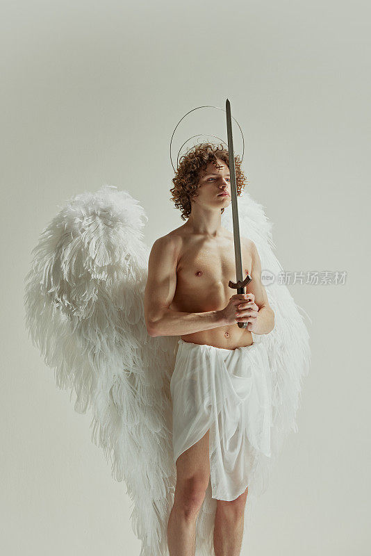 男子手持剑，他的翅膀像天使一样展开，模特看着侧面，在白色的工作室背景下体现了英勇和优雅。