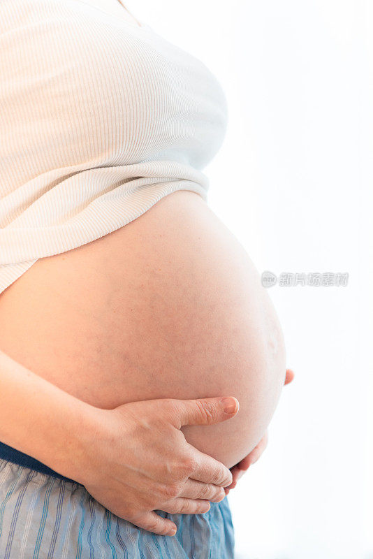 一个孕妇抱着肚子站在窗边