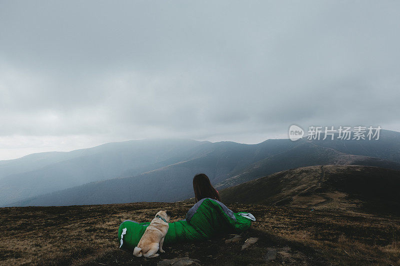 睡袋里的女人和狗在山中醒来