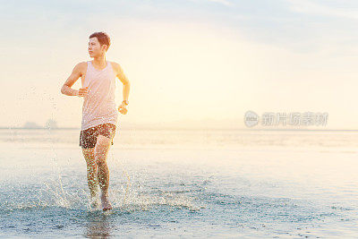 年轻的亚洲男子在海滩上奔跑，夕阳为背景