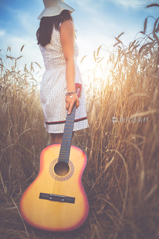 拿着吉他的女人走过高高的草丛。