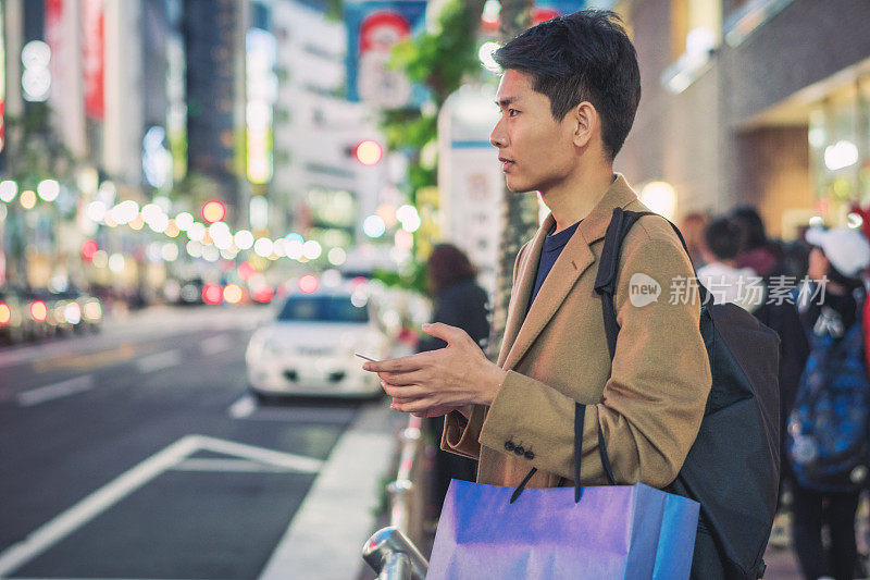 在日本，一名年轻的亚洲男子在购物中心或百货公司购买圣诞礼物时，一边使用手机一边寻找圣诞礼物