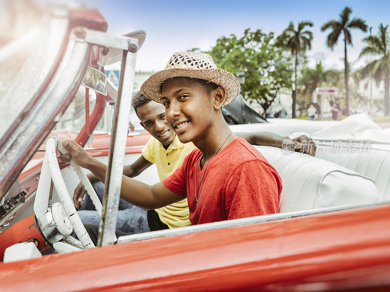 两个年轻的古巴人开着红色敞篷车在古巴老城哈瓦那