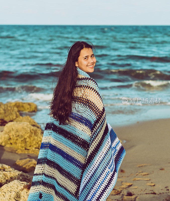 舒适的海滩，年轻女子裹着毯子躺在沙滩上