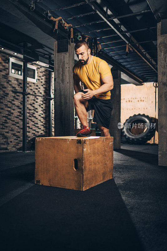 活跃的男运动员在一个木板条箱上做踏步运动，同时在健身房进行健身训练