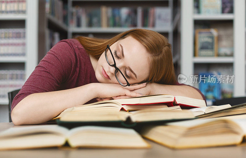 戴眼镜的疲惫女孩在图书馆的书上打盹
