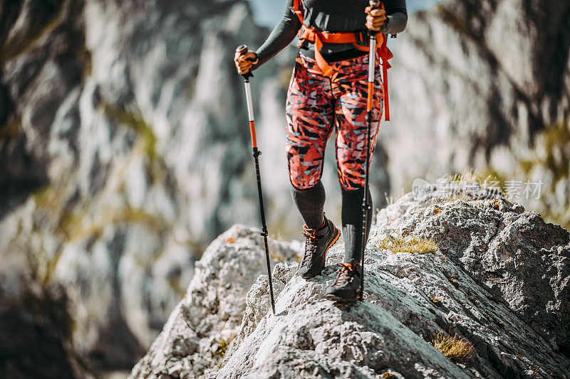 腰部以下的观点，一个女登山家正在翻越狭窄的岩石脊在山上