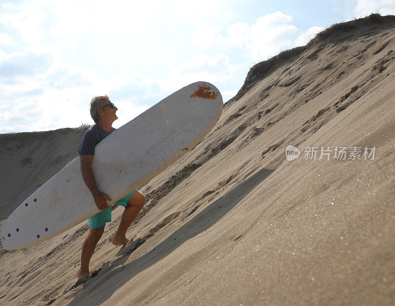 男人扛着冲浪板爬上沙丘