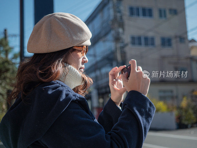 美丽的年轻女孩在城市里用智能手机拍照。