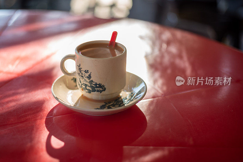 红桌子上放着马来西亚热奶茶，用老式的玻璃杯和茶碟