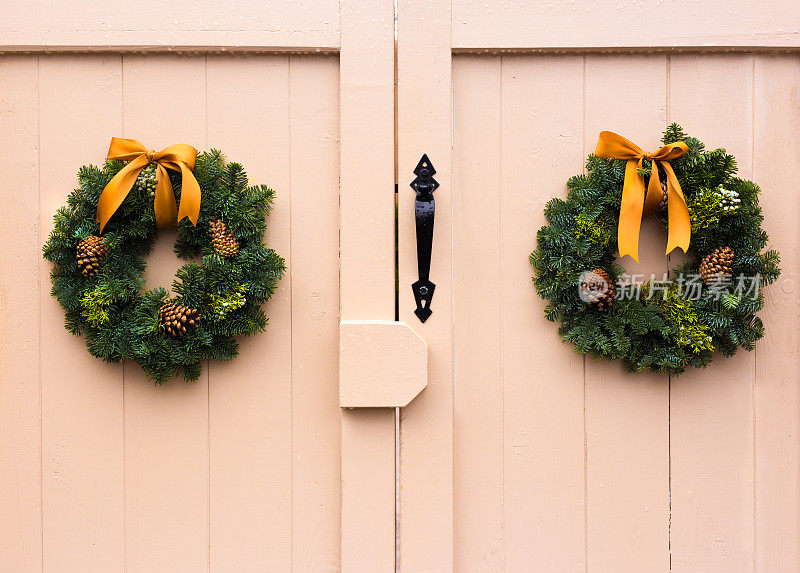 两个绿色的圣诞花环在乡村的门上，黄色的弓
