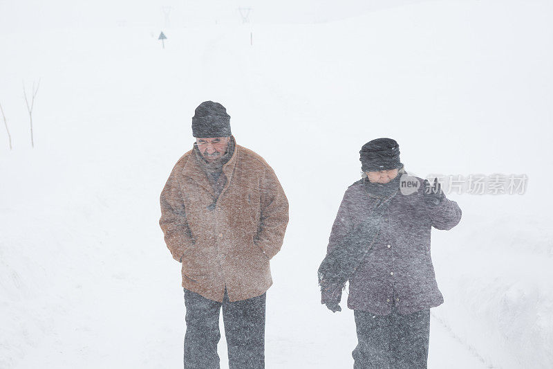 一对老年夫妇在下雪的乡村路上穿着暖和的衣服