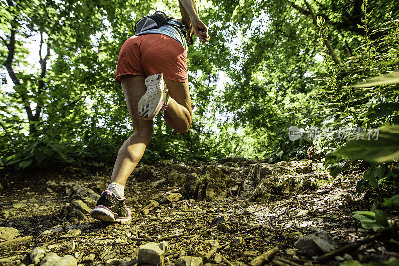 女性跑步者在岩石森林小路上坡