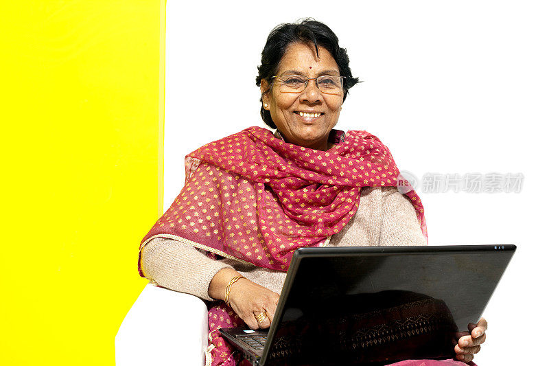 愉快的印度老妇人用笔记本电脑工作