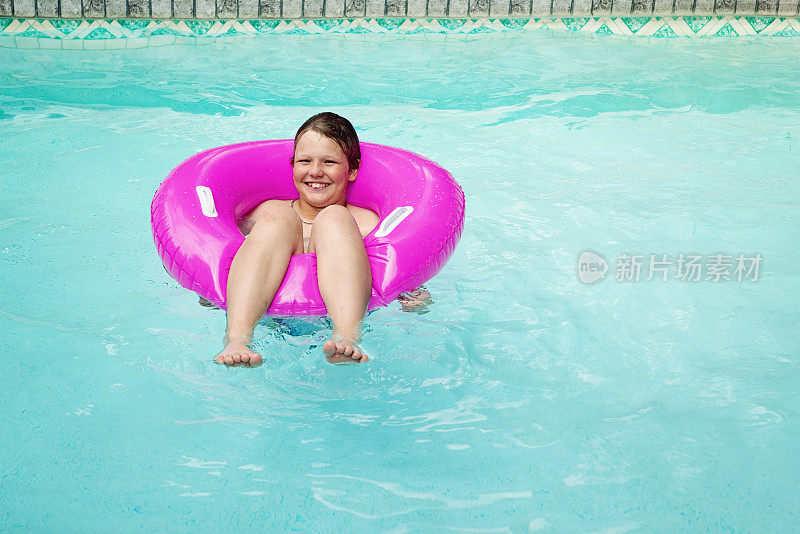 小男孩在游泳池里放松，粉红色的大塑料浮动。