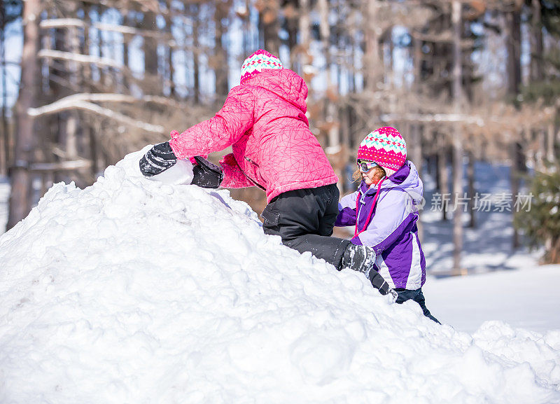 两个小女孩冬天在雪堆上玩