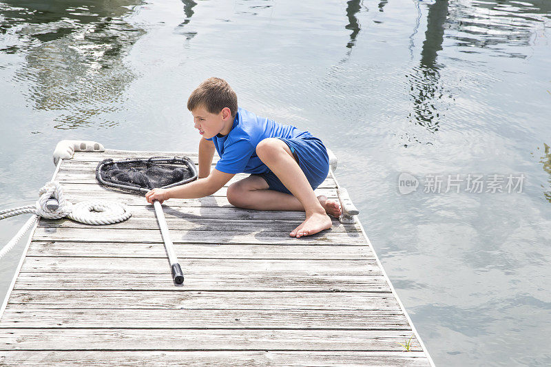 一个白人男孩坐在码头上拿着渔网