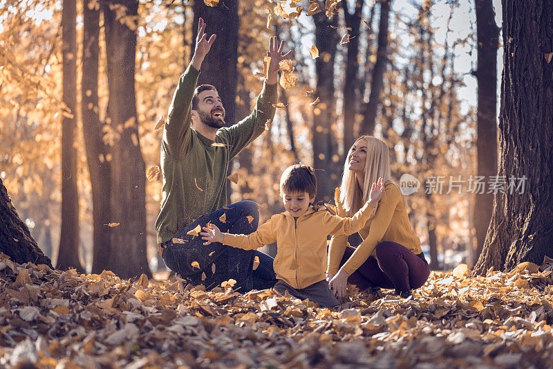 幸福的夫妇和他们的儿子在公园里玩秋天的树叶