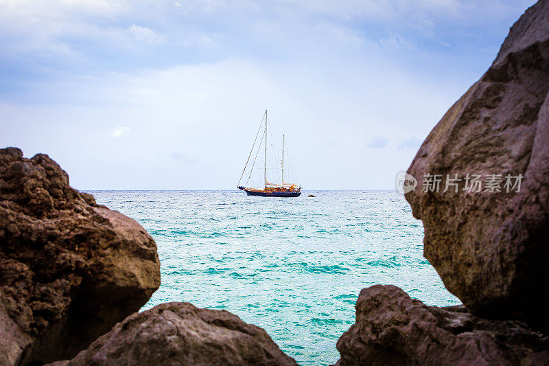 意大利西西里岛海上的一艘帆船。在前景中，散焦的熔岩石