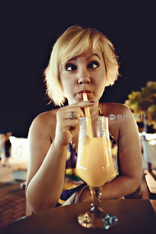 有趣的肖像斜视金发女人的眼睛，而喝她的果汁在晚上在花园的咖啡。