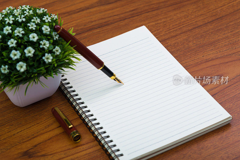 钢笔或墨水笔与笔记本纸和小装饰树在白色花瓶上的木制工作台与复印空间，办公桌的概念。