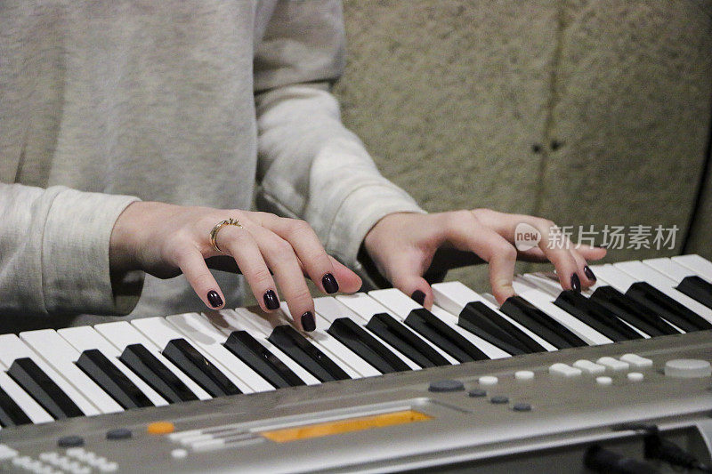 一位年轻的钢琴家弹奏着她最喜欢的音乐的电子钢琴。女性优雅的手触摸键盘的合成器特写。