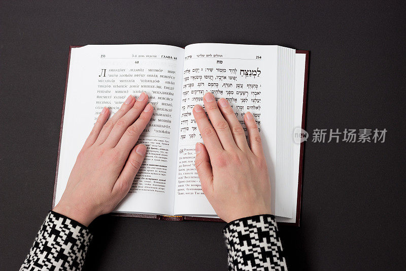 犹太书，女人的手，在黑色背景上。希伯来文，祈祷。女人用书祈祷。