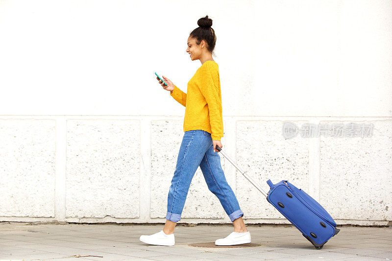 年轻女子走路带着旅行袋和使用手机