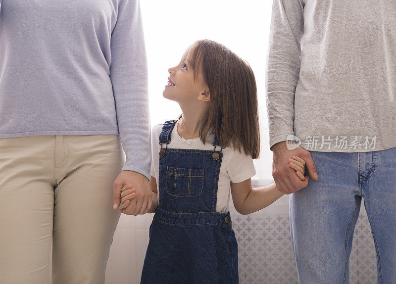 可爱的小女孩牵着父母的手，仰望着妈妈