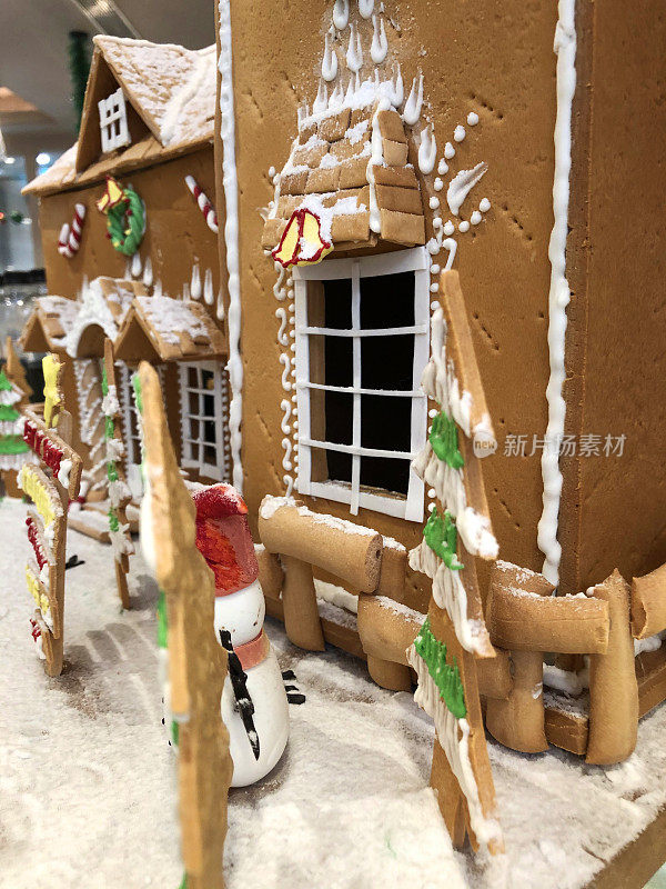 这是自制的姜饼饼干屋的特写，在厨房的工作台上用糖霜和糖果糖果装饰，圣诞树和雪人雕像
