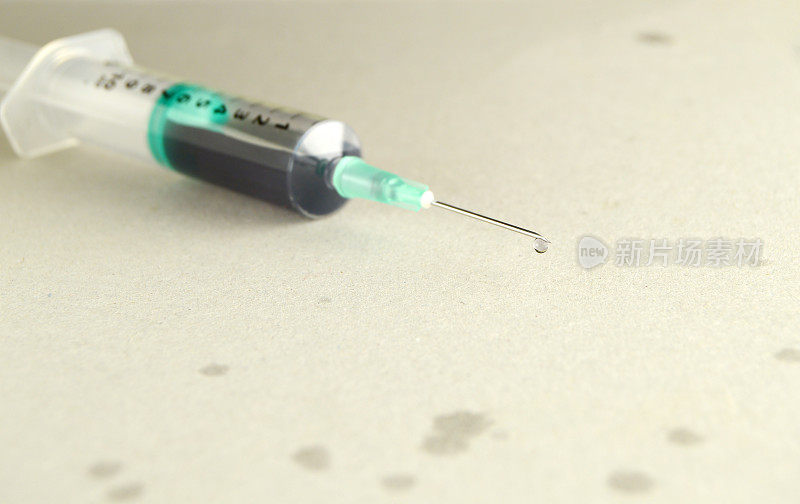 近距离观察一个充满药液的医疗注射器，有一滴药液从针头中渗出