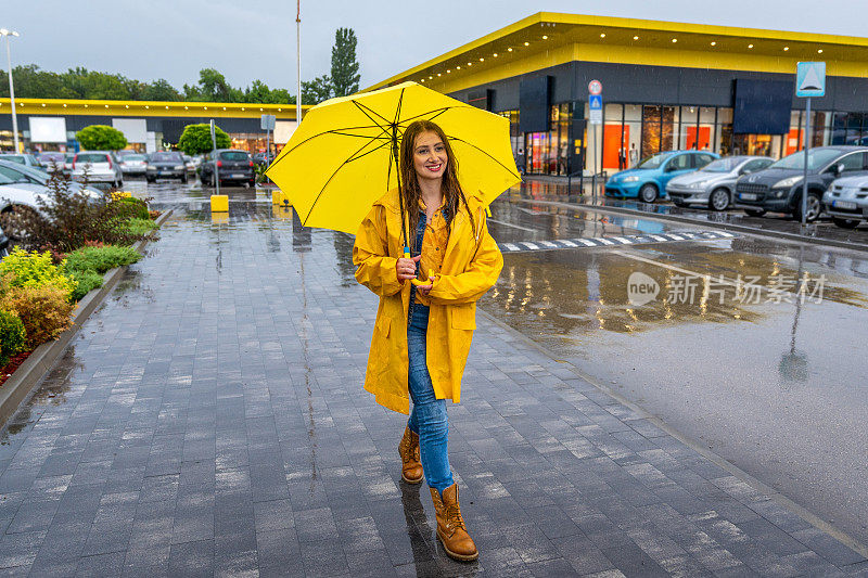 年轻女子撑着黄伞在雨中行走