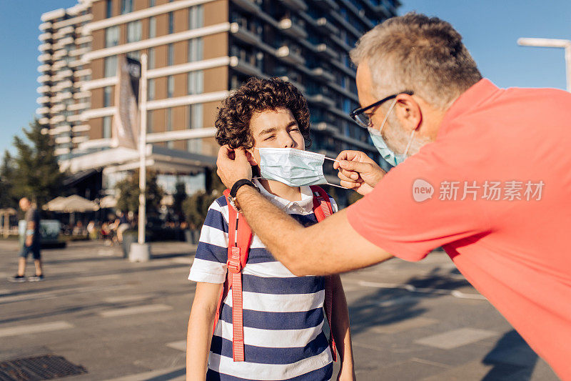 男孩和他的父亲站在街上，戴着口罩在上学的路上