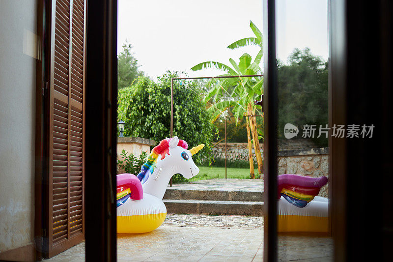 一个充气彩虹独角兽的照片，通过开放的露台门拍摄在前门廊