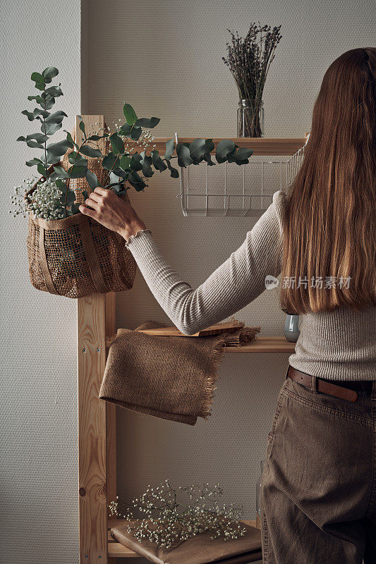 女孩用一个用桉树枝、花和室内植物装饰的环保袋装饰了一个木架子。生态化实例、存储。民间。